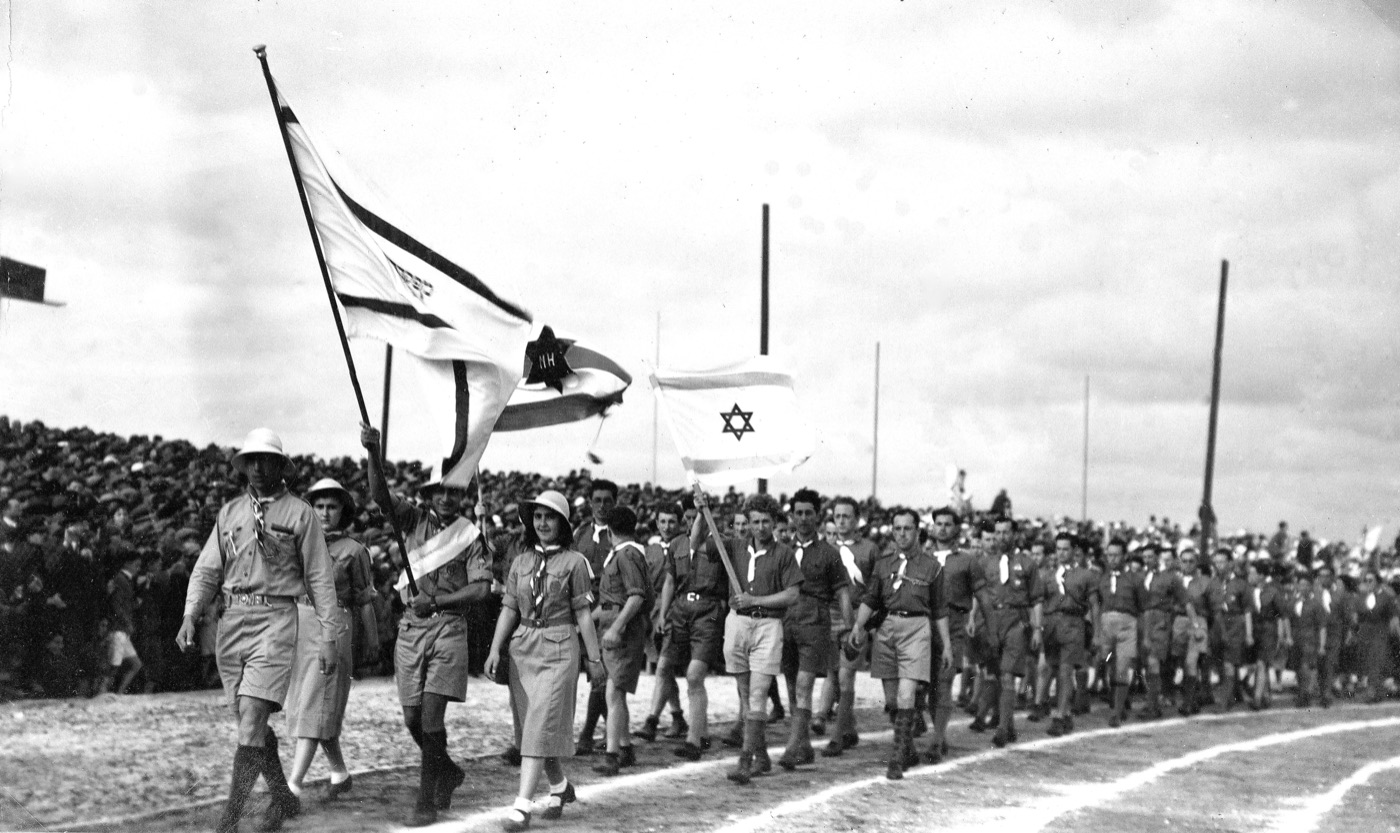 The Eretz Yisrael delegation parading into the stadium at the opening ceremony of the 2nd Maccabiah Games, Tel Aviv, 2 April 1935. The athletes march in a long column behind their team banner; the surrounding stand and field furniture are British Mandate civic architecture.