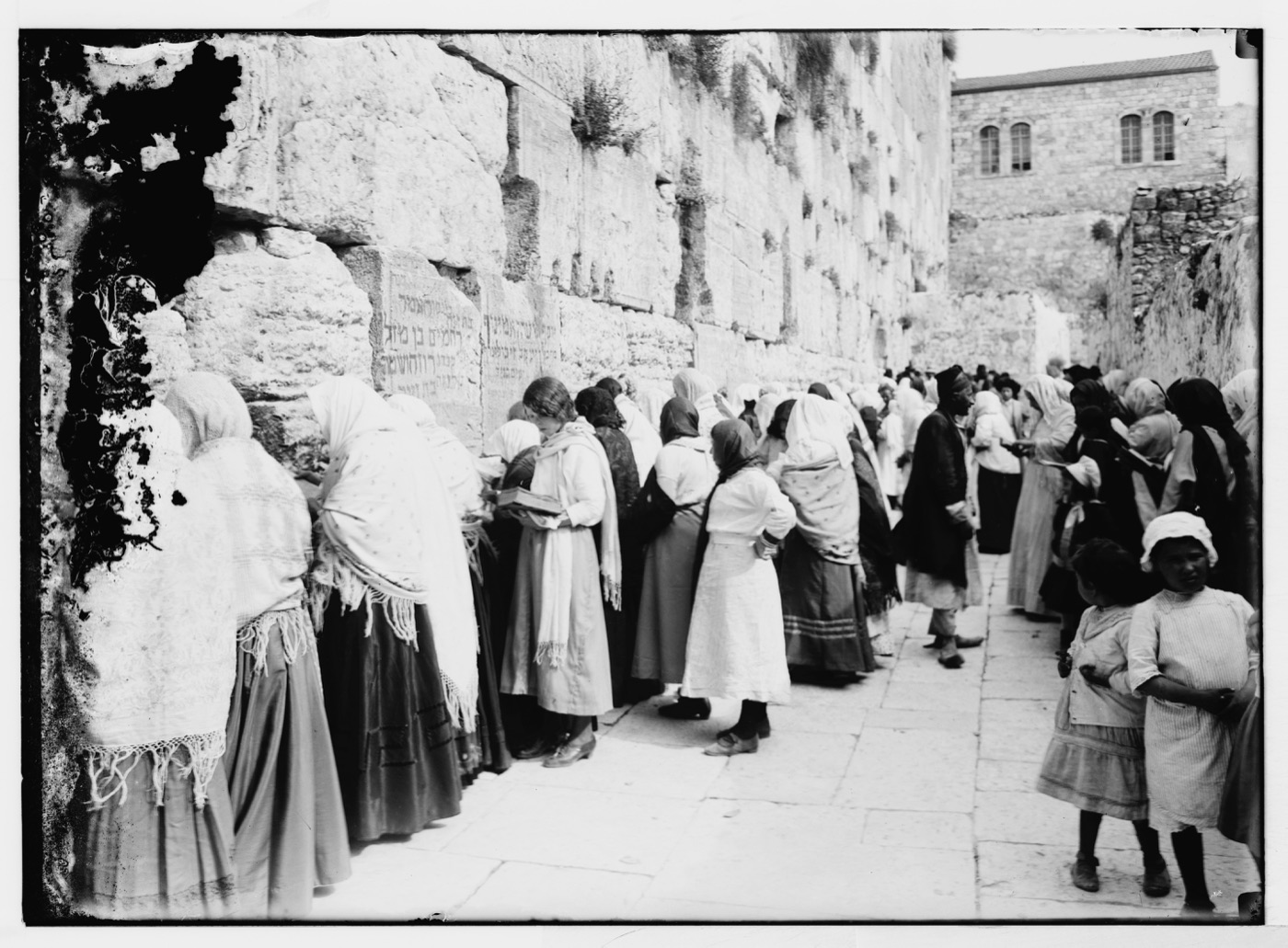 Jews praying at the Western Wall in Jerusalem under the British Mandate. A row of worshippers in Eastern European dress stand facing the ashlar masonry of the Wall; a few seated figures read from books in their laps. Photograph from the Matson Photograph Collection, Library of Congress.